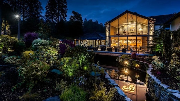 A modern house with a glass facade, surrounded by a landscaped garden and a pond. - Langdale Hotel  (Ambleside)