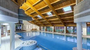 An indoor swimming pool with a wooden ceiling, clear glass windows, and a seating area with chairs. - Langdale Hotel  (Ambleside)