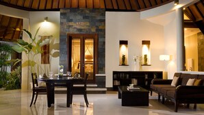 A spacious living area with a dining table, sofas, and a fireplace. - The Kunja (Seminyak)