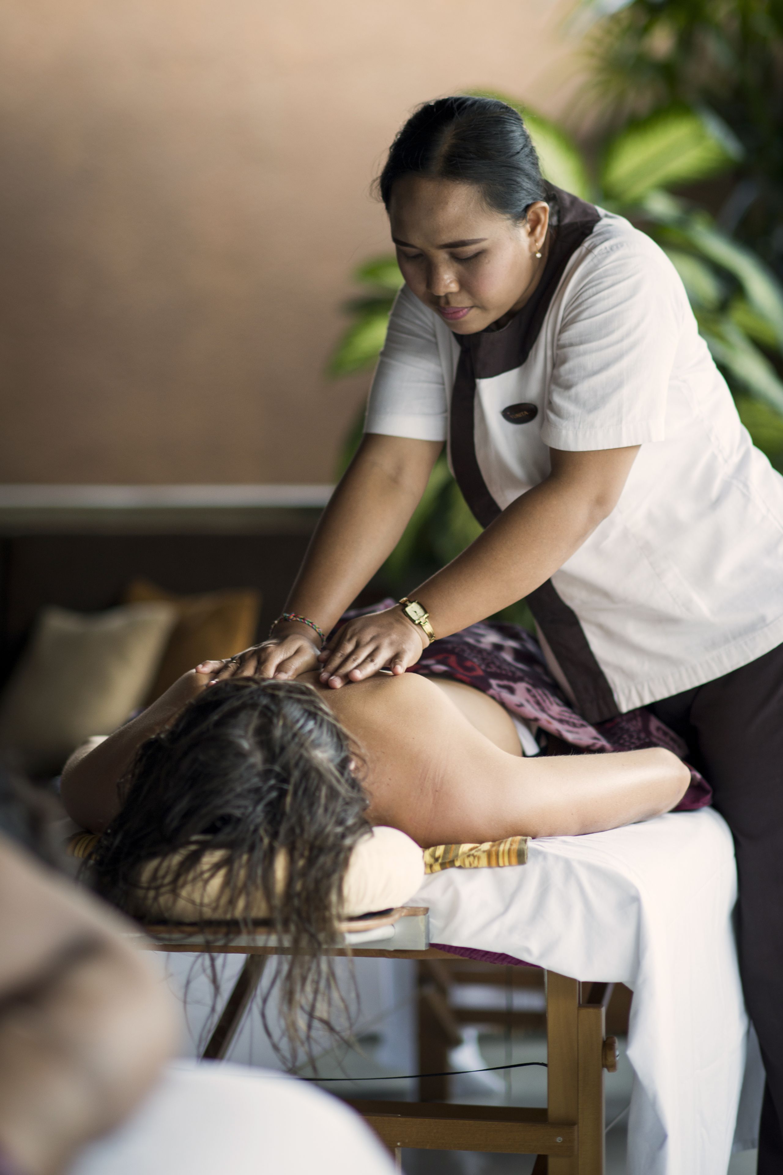 A massage therapy session in a room with a massage table, a person receiving the massage, and a therapist.