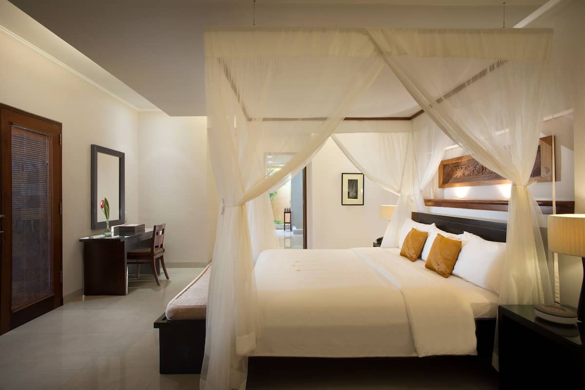 A bedroom with a bed, bedside table, chair, desk, and a desk lamp.