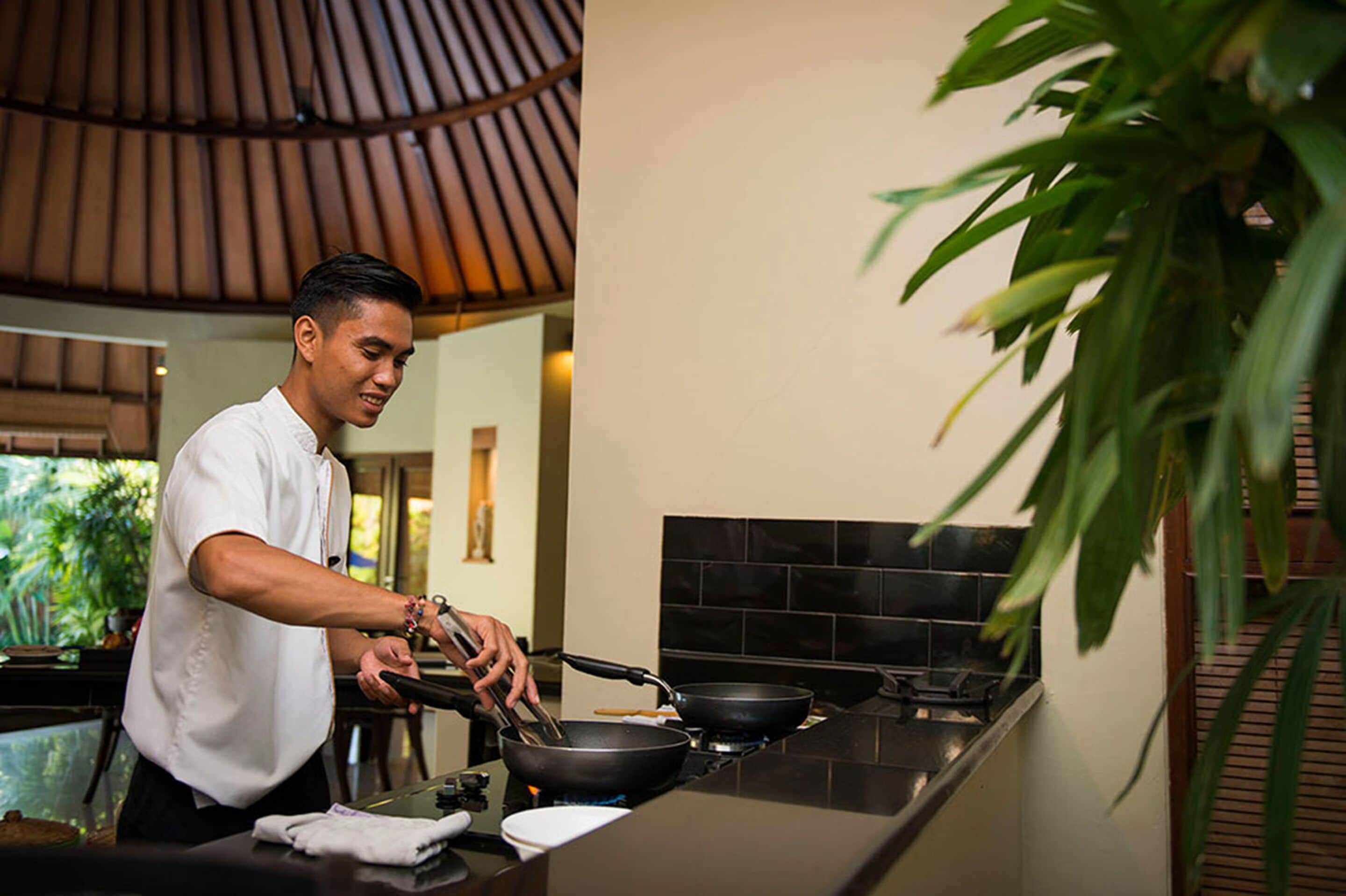 A chef cooking in a modern kitchen with a black tiled backsplash and a wooden ceiling.