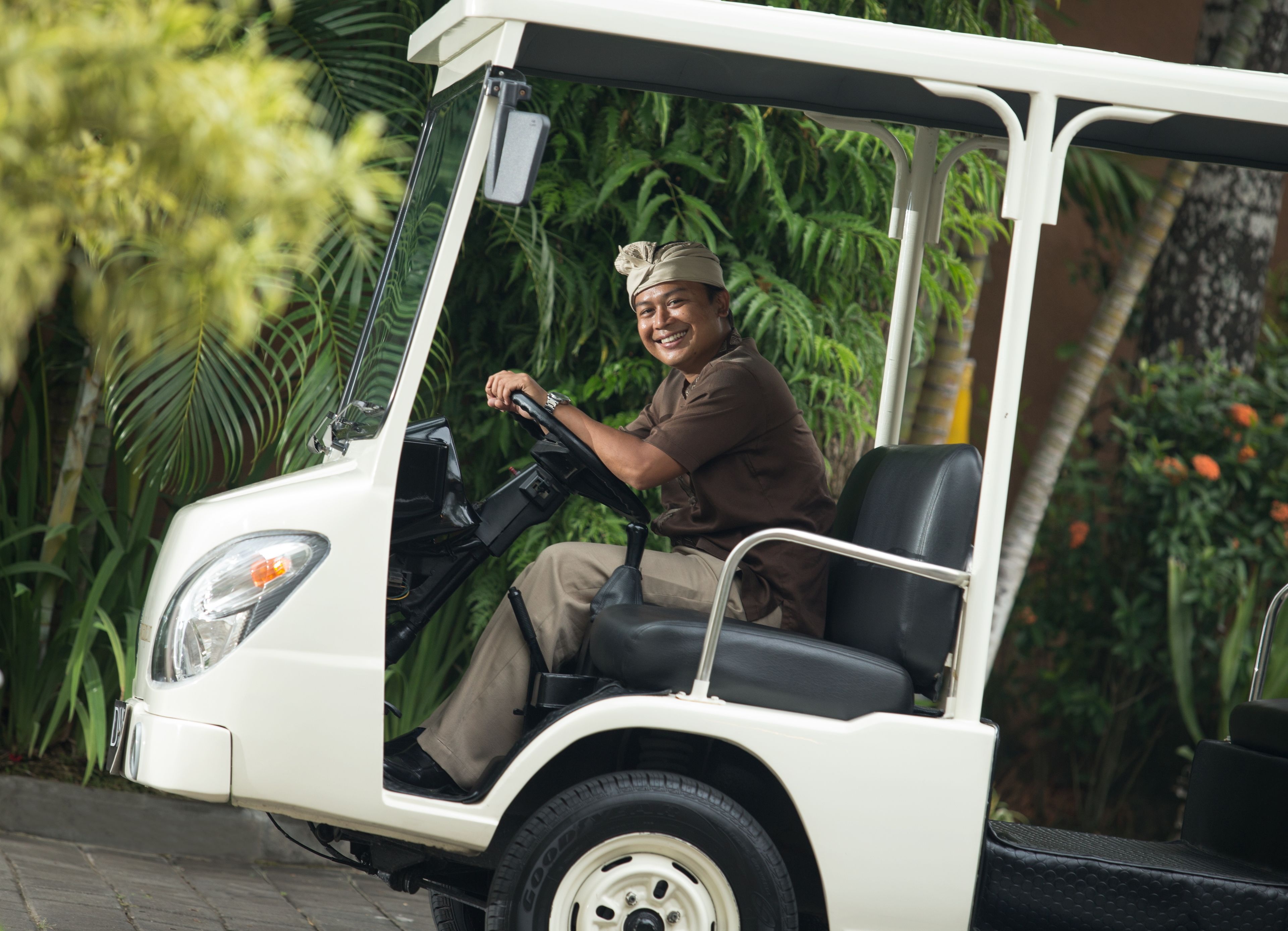 A golf cart with a driver, surrounded by lush greenery.