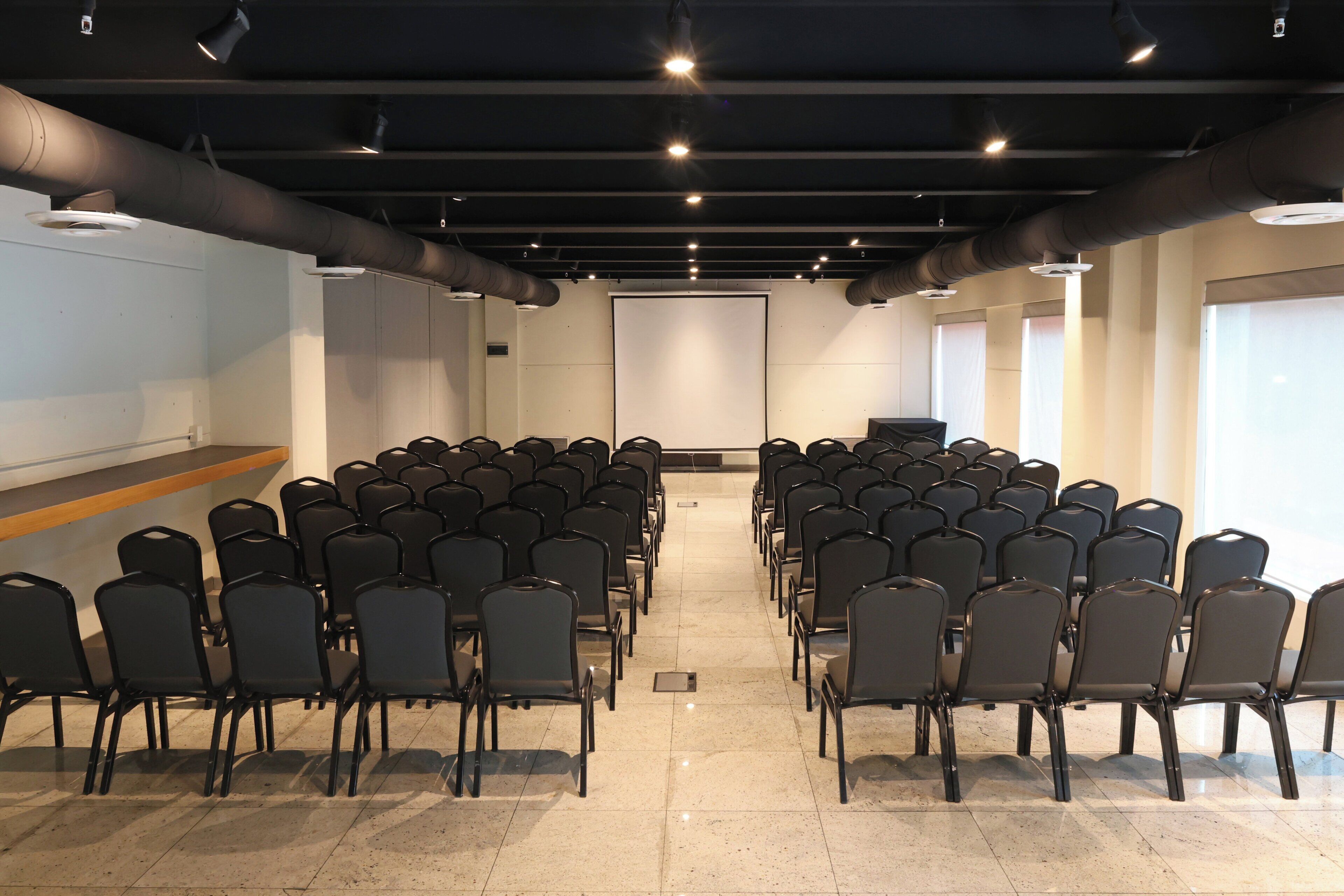 A conference room with rows of chairs, a podium, and a large screen at the front.