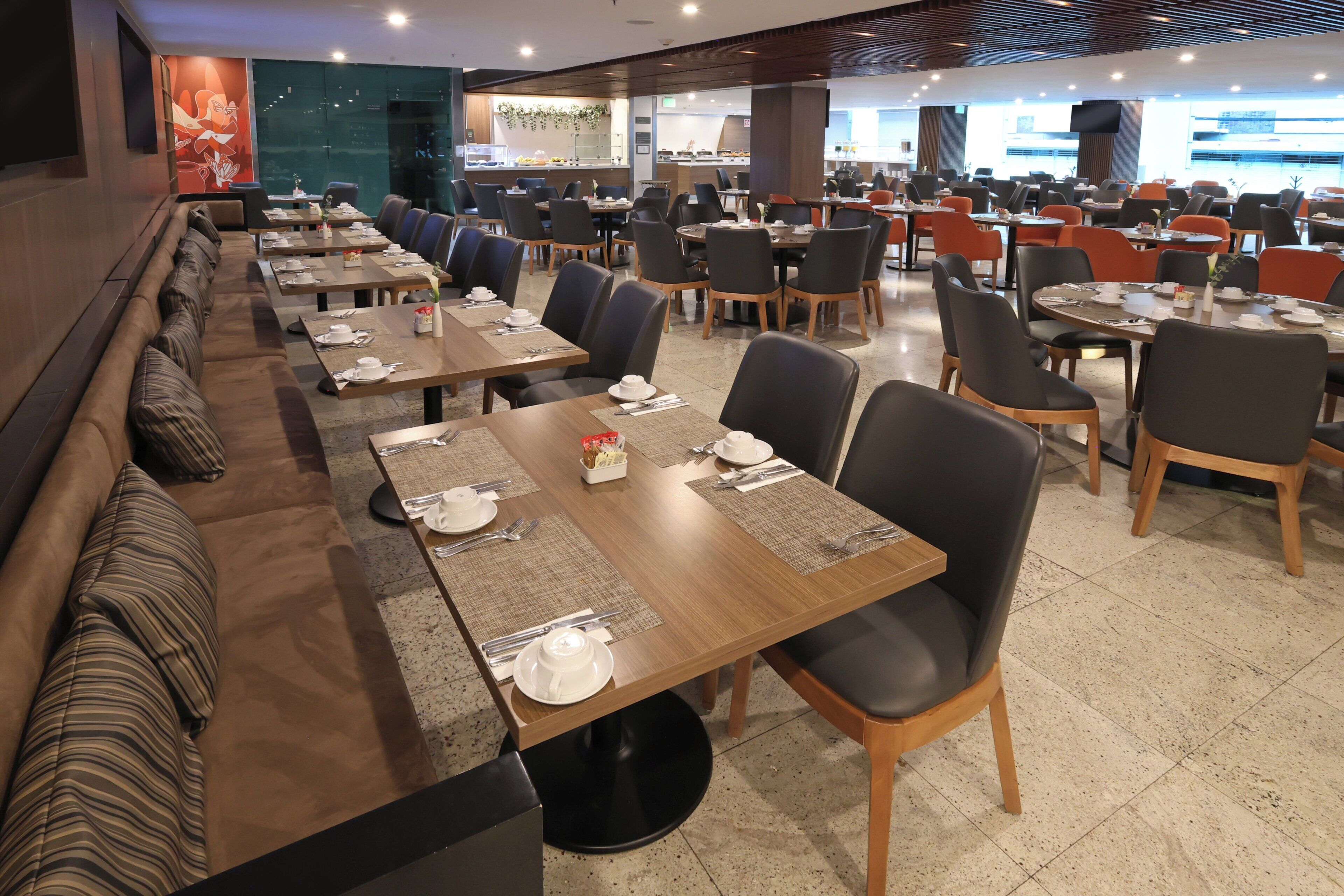Een ruime eethoek met meerdere tafels en stoelen, een lange bank en een keuken in de achtergrond.