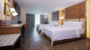 Habitación de hotel con dos camas, un escritorio, una silla y una lámpara de escritorio.