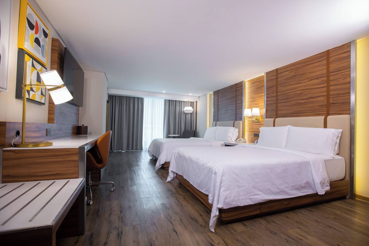 Habitación de hotel con dos camas, un escritorio, una silla y una lámpara de escritorio.
