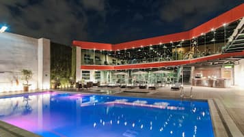 A modern building with a swimming pool, outdoor seating, and a covered area with exercise equipment.