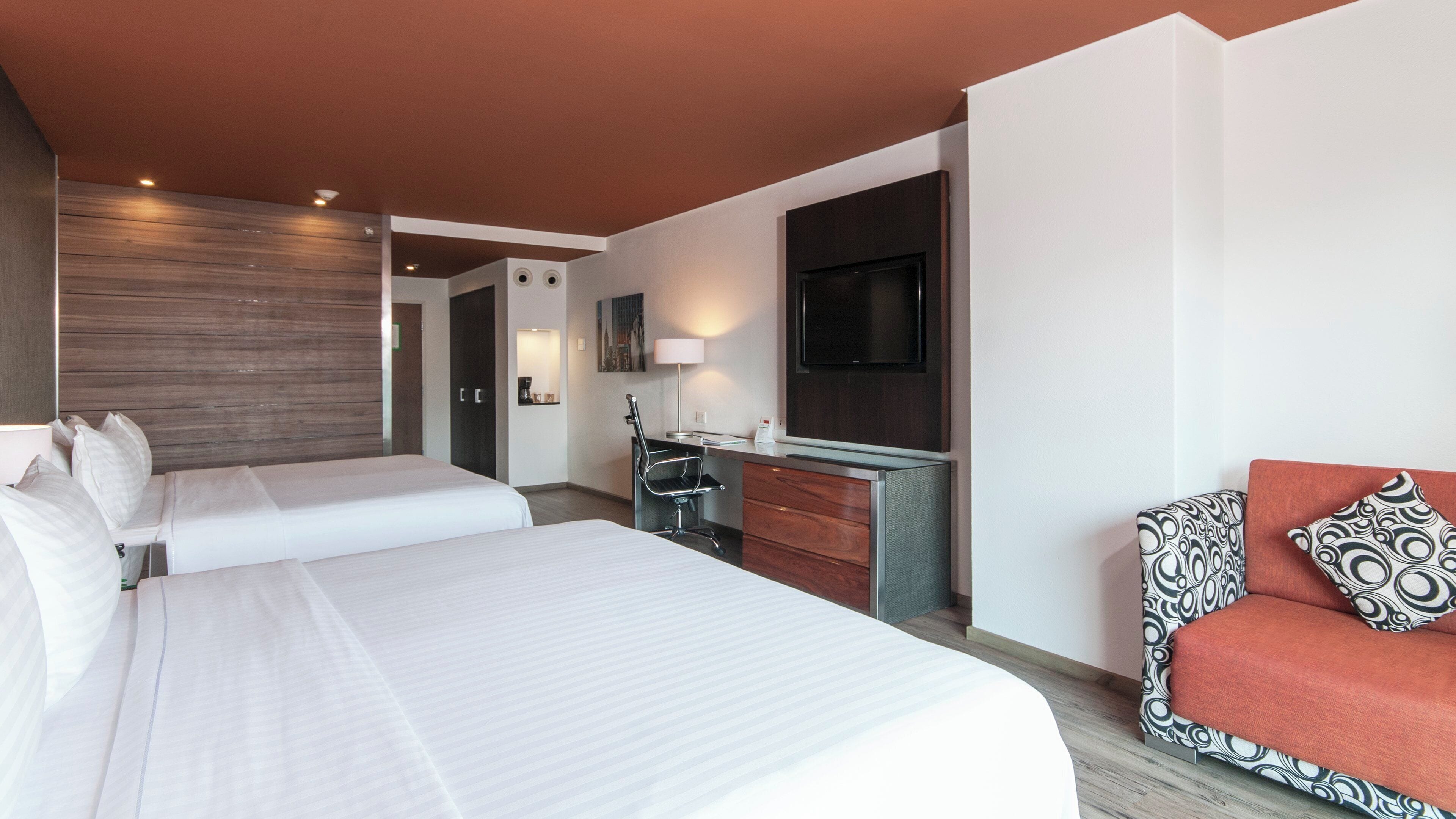 Une chambre d’hôtel avec deux lits, un bureau, une chaise, une télévision et un canapé.