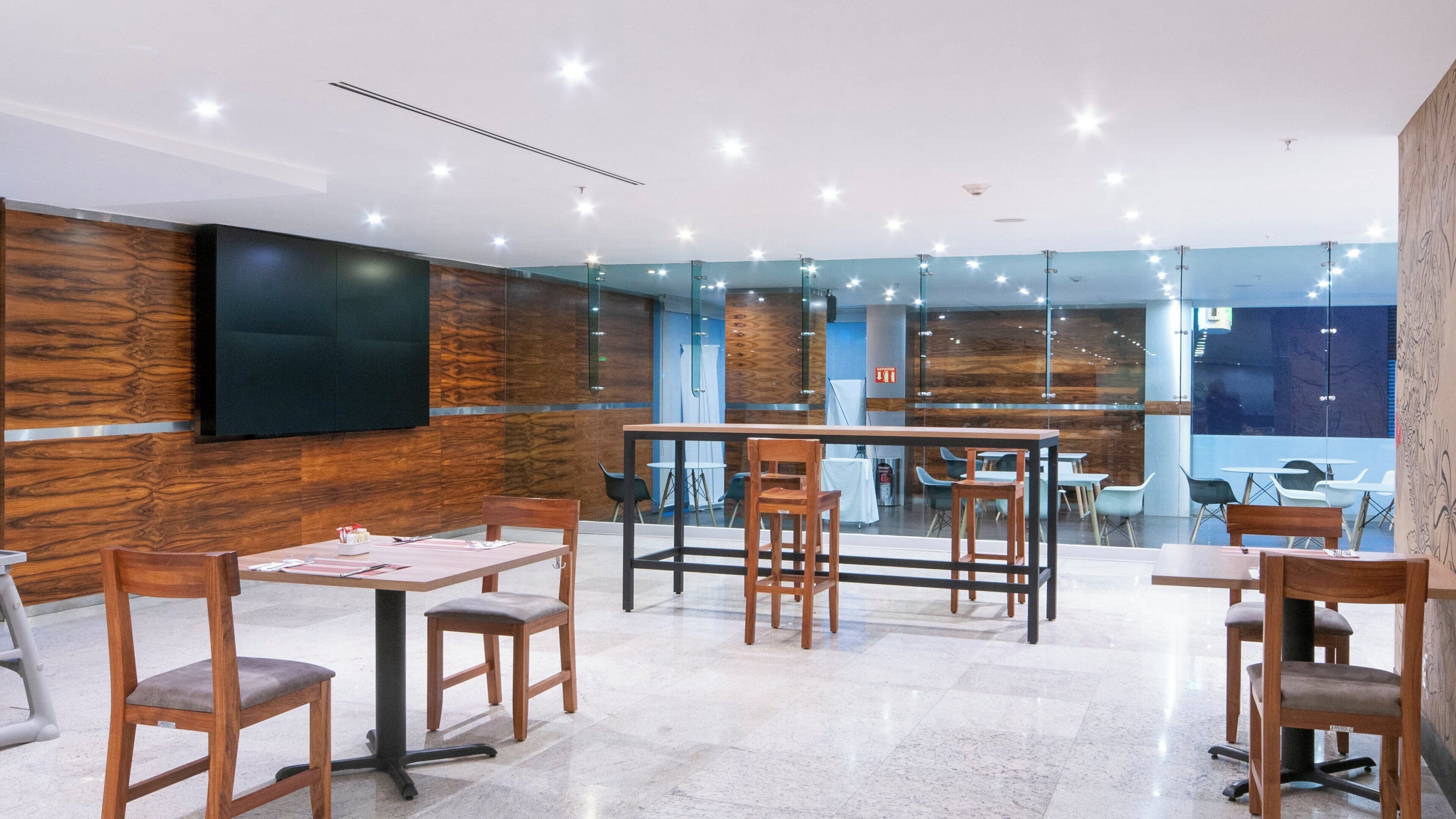 A modern interior with wooden panel walls, a flat-screen TV mounted on the wall, and multiple tables and chairs arranged for dining.