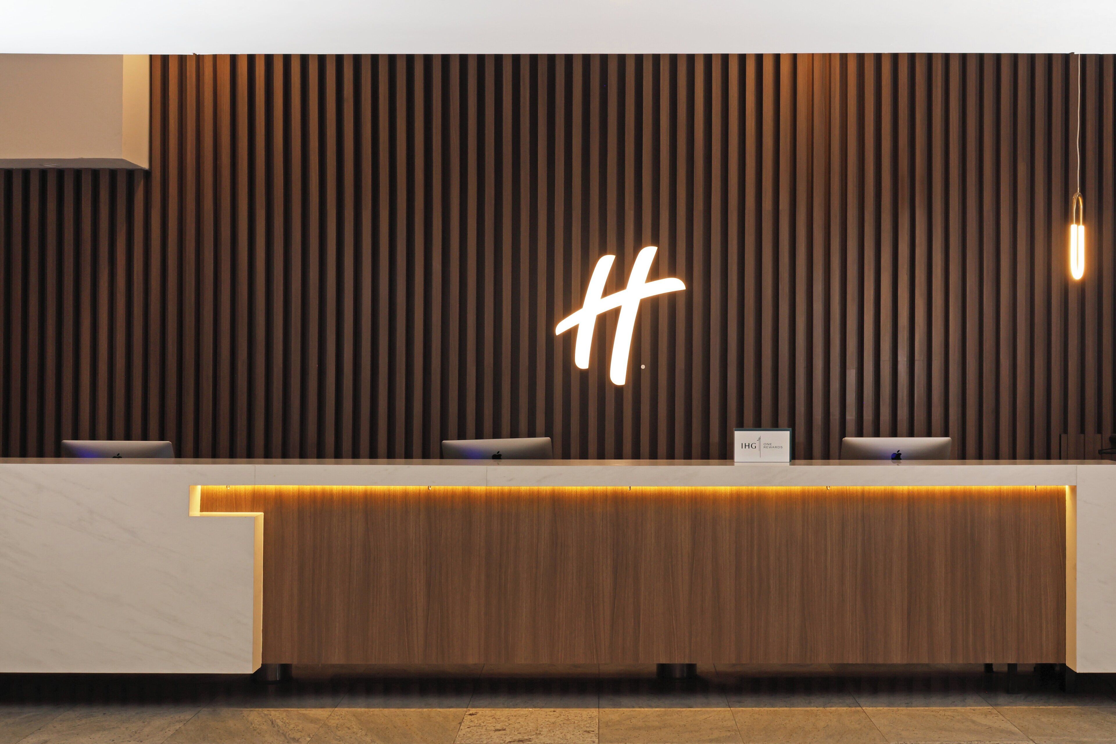 Un mostrador de recepción con un panel de madera de fondo y un letrero de neón con la letra 'H'.