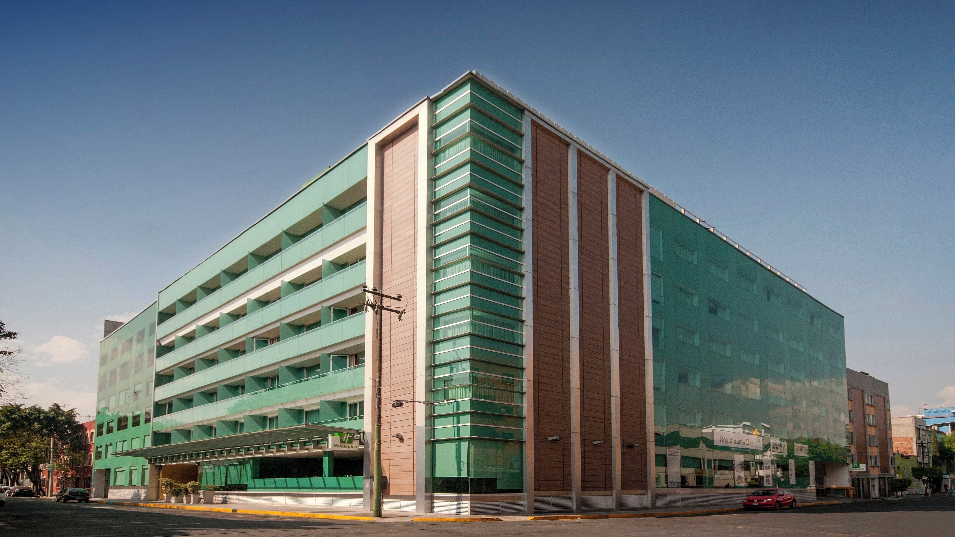 Un hotel de varios pisos con fachada verde y un bar restaurante visible en la planta baja.
