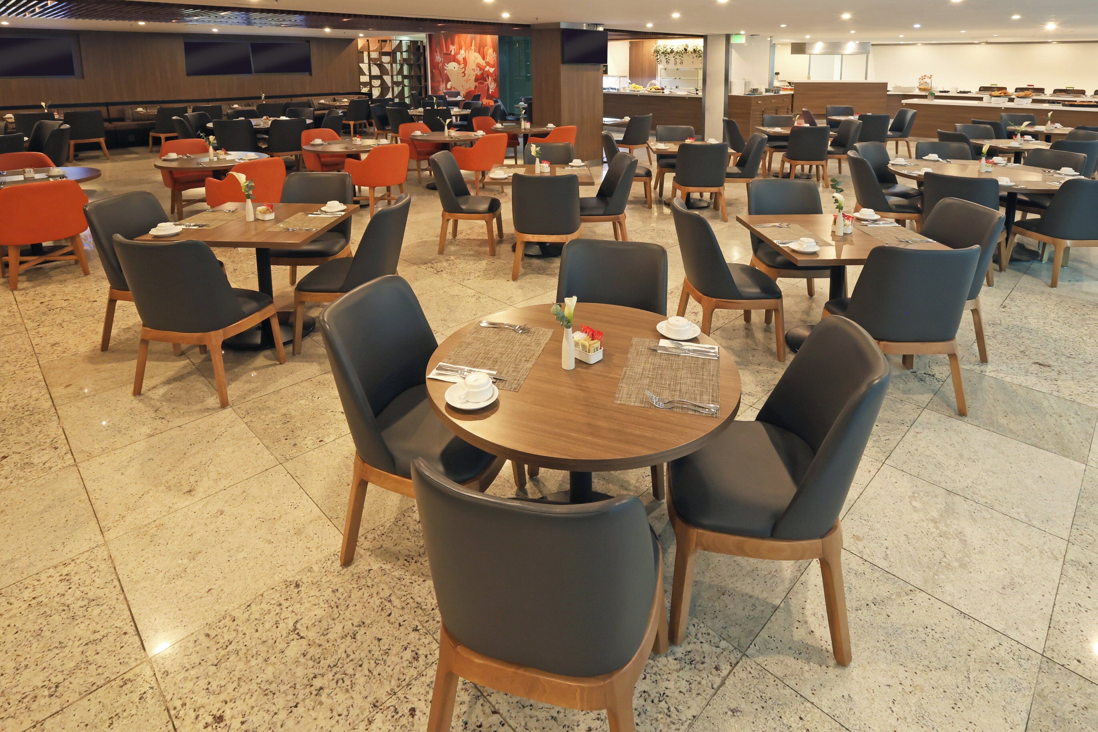 Un comedor amplio con varias mesas y sillas, una cocina al fondo y un diseño de interiores moderno.
