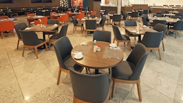 Un comedor amplio con varias mesas y sillas, una cocina al fondo y un diseño de interiores moderno.