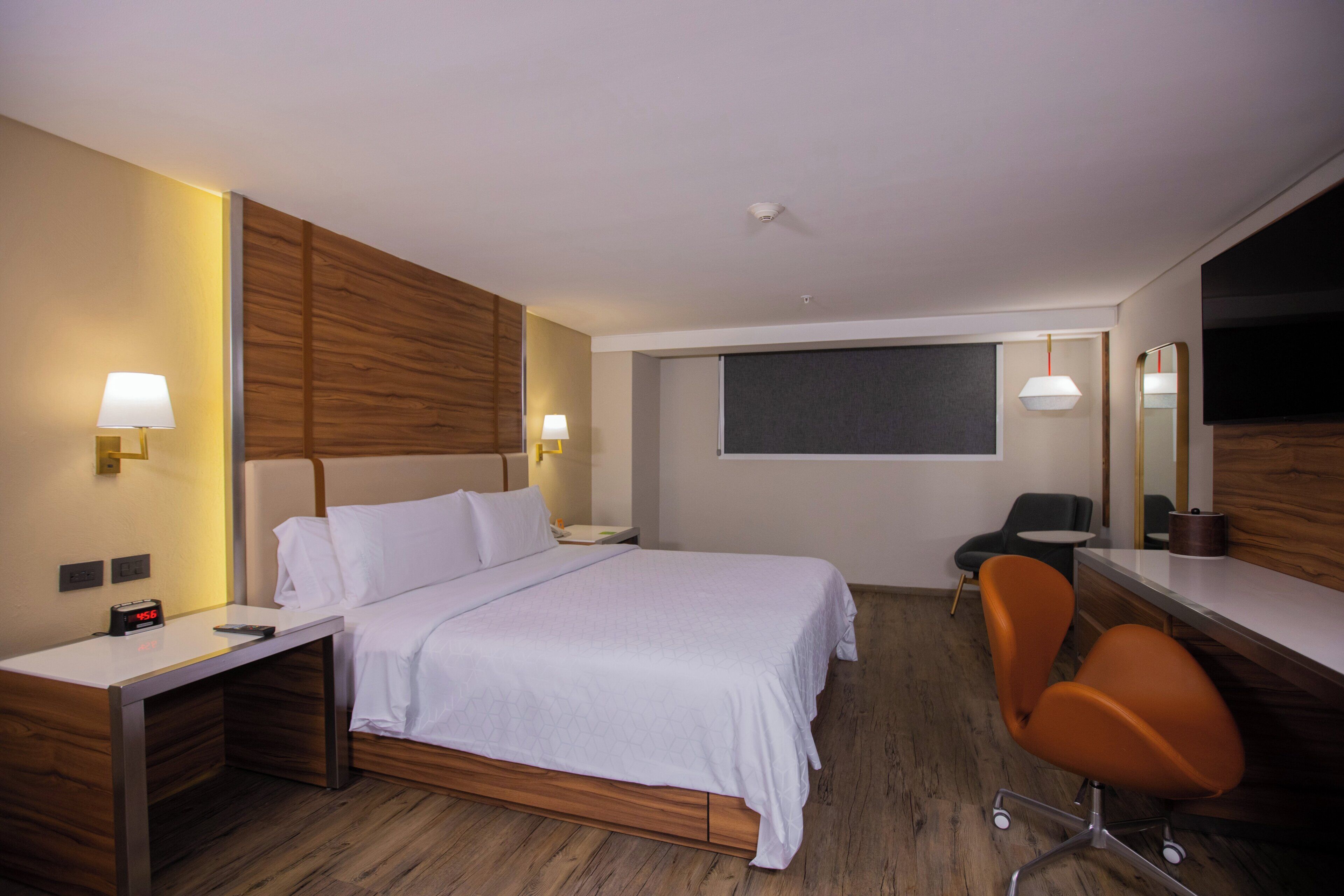 Ein Hotelzimmer mit Bett, Schreibtisch, Stuhl und einem großen Spiegel.