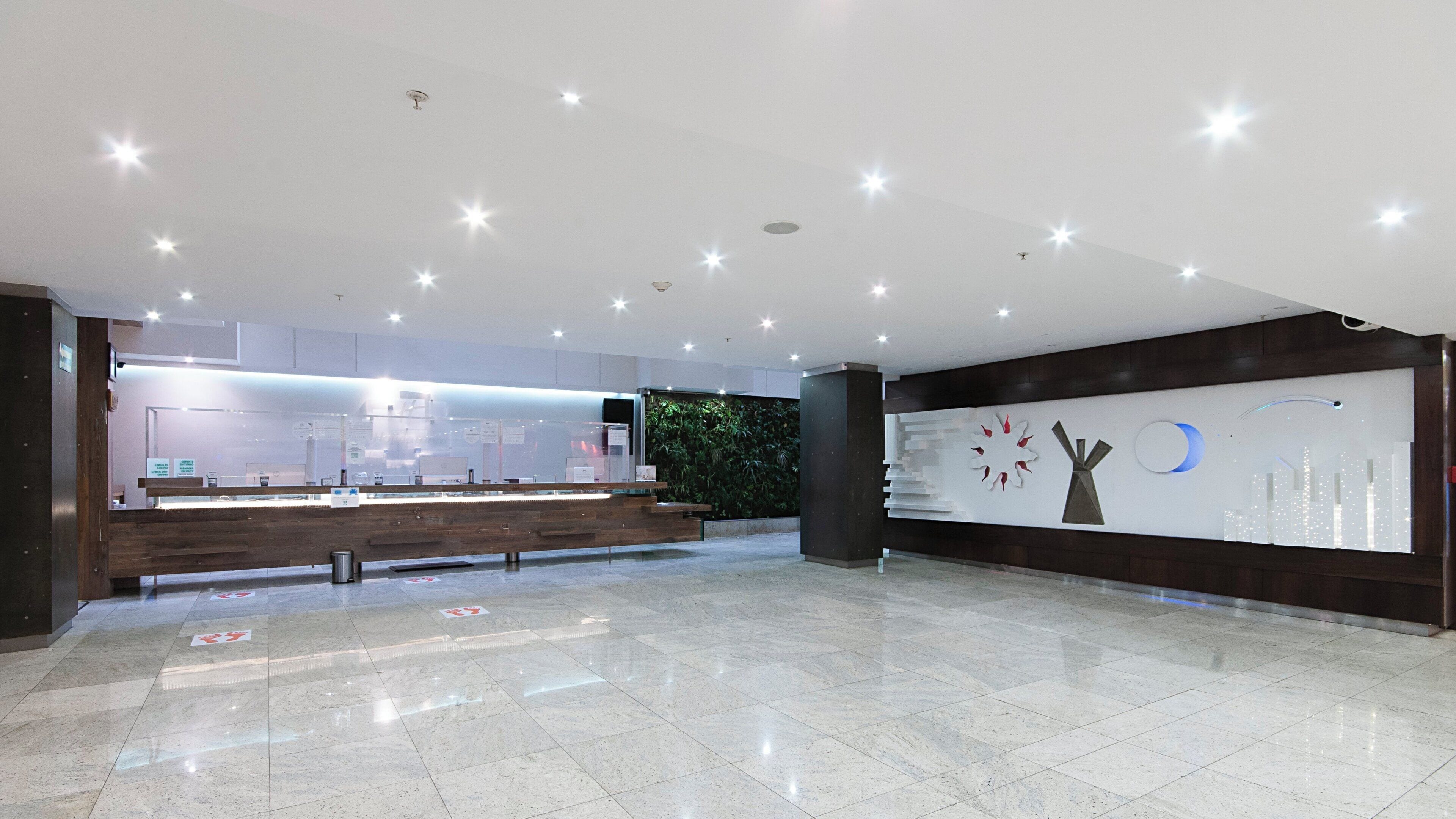 A modern reception area with a wooden reception desk, a green wall, and a decorative wall piece.