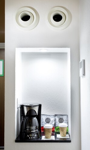 Een koffieapparaat met twee koffiekapsules en twee wegwerpbekers op een zwart aanrecht.