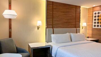 A hotel room with a bed, a chair, a small table, and two wall-mounted lamps.