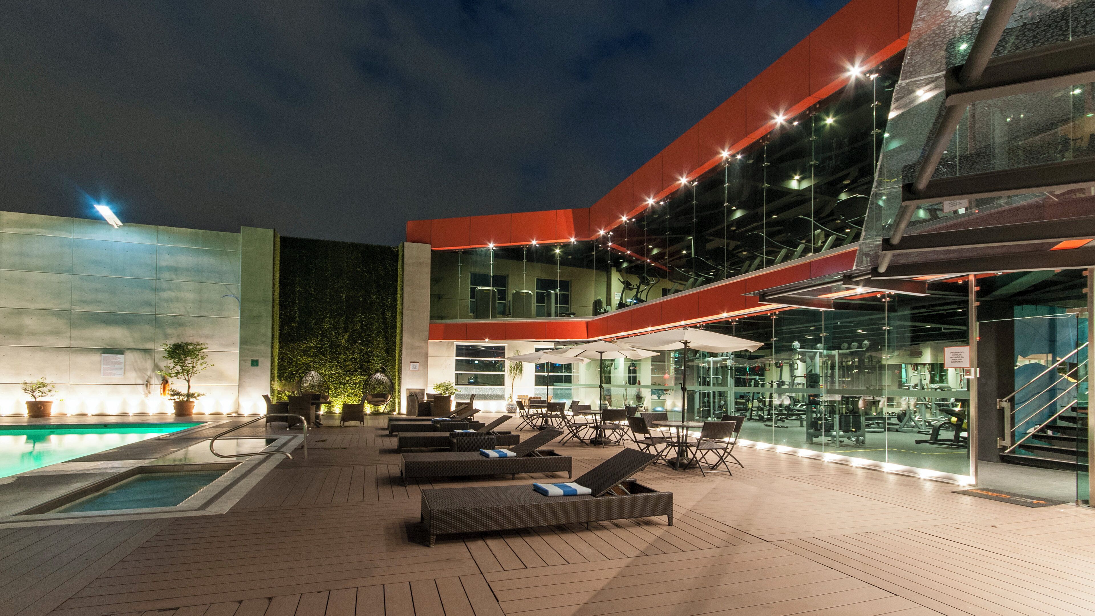An outdoor pool area with lounge chairs and umbrellas, surrounded by a modern building with glass walls.