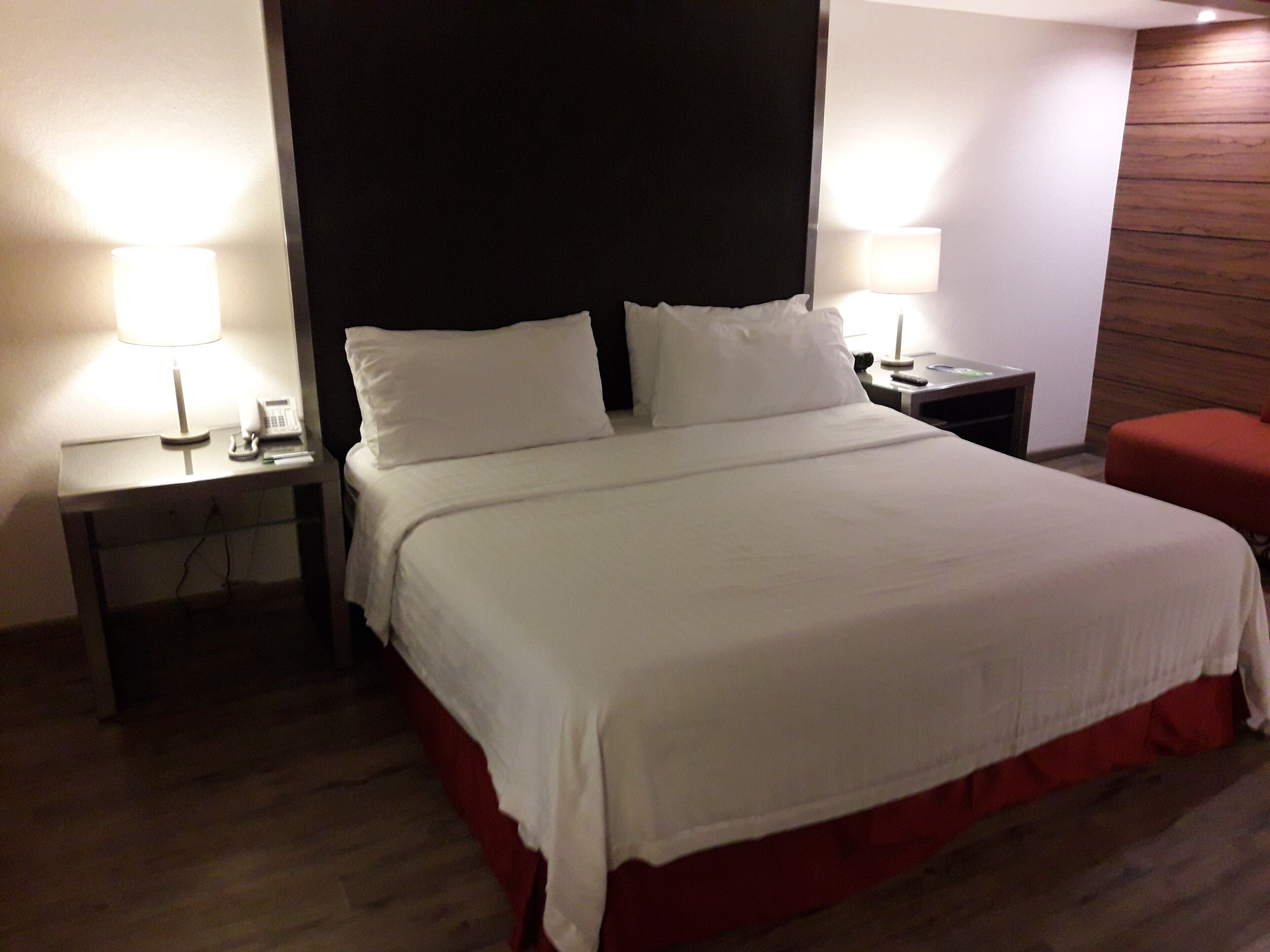 Une chambre d’hôtel avec un lit, deux tables de chevet, une petite table, une chaise rouge et un mur d’accent en bois.
