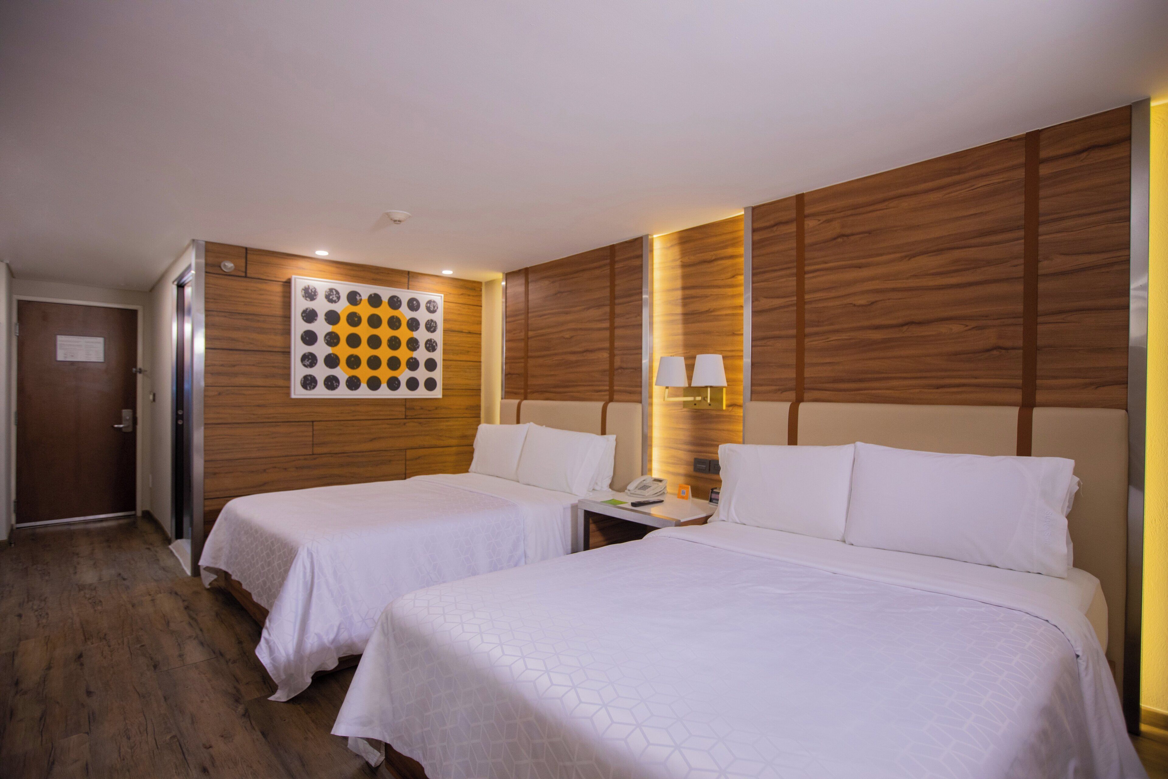 Une chambre d’hôtel avec deux lits, un lambris en bois, une œuvre d’art murale, une table de chevet avec une lampe et une porte.