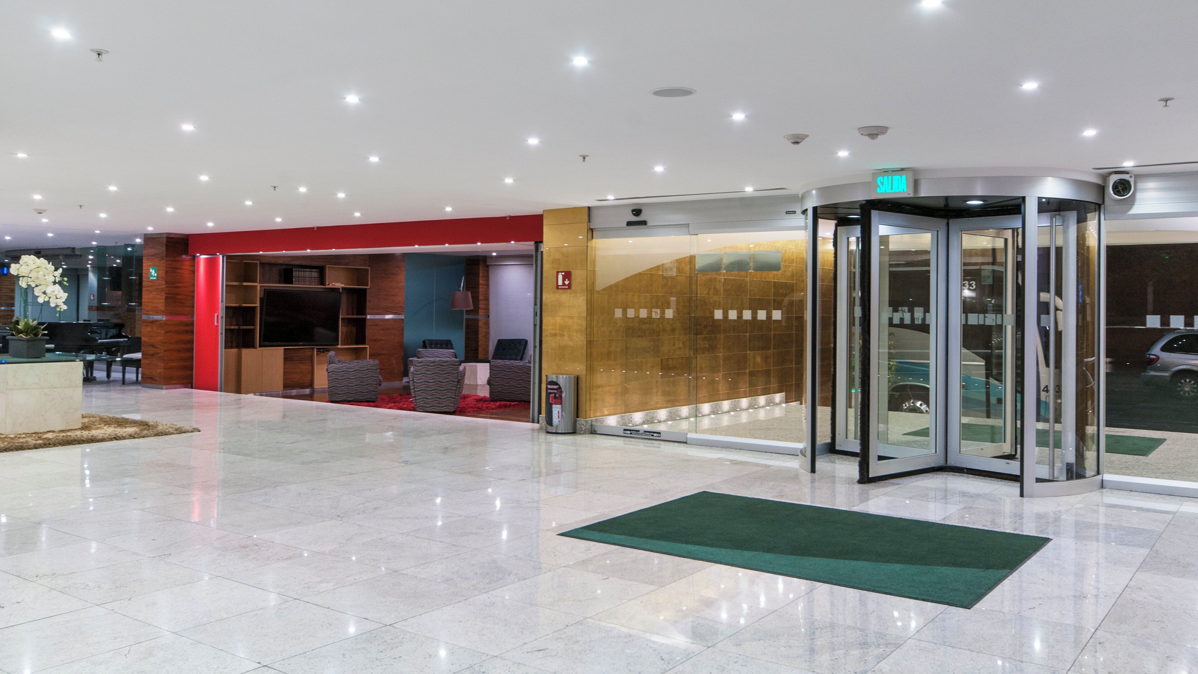 Un hall d’hôtel doté d’une porte tournante, d’un comptoir de réception et d’un espace détente avec des canapés.