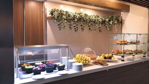 Un comptoir de buffet proposant divers plats, une vitrine réfrigérée et une plante décorative.