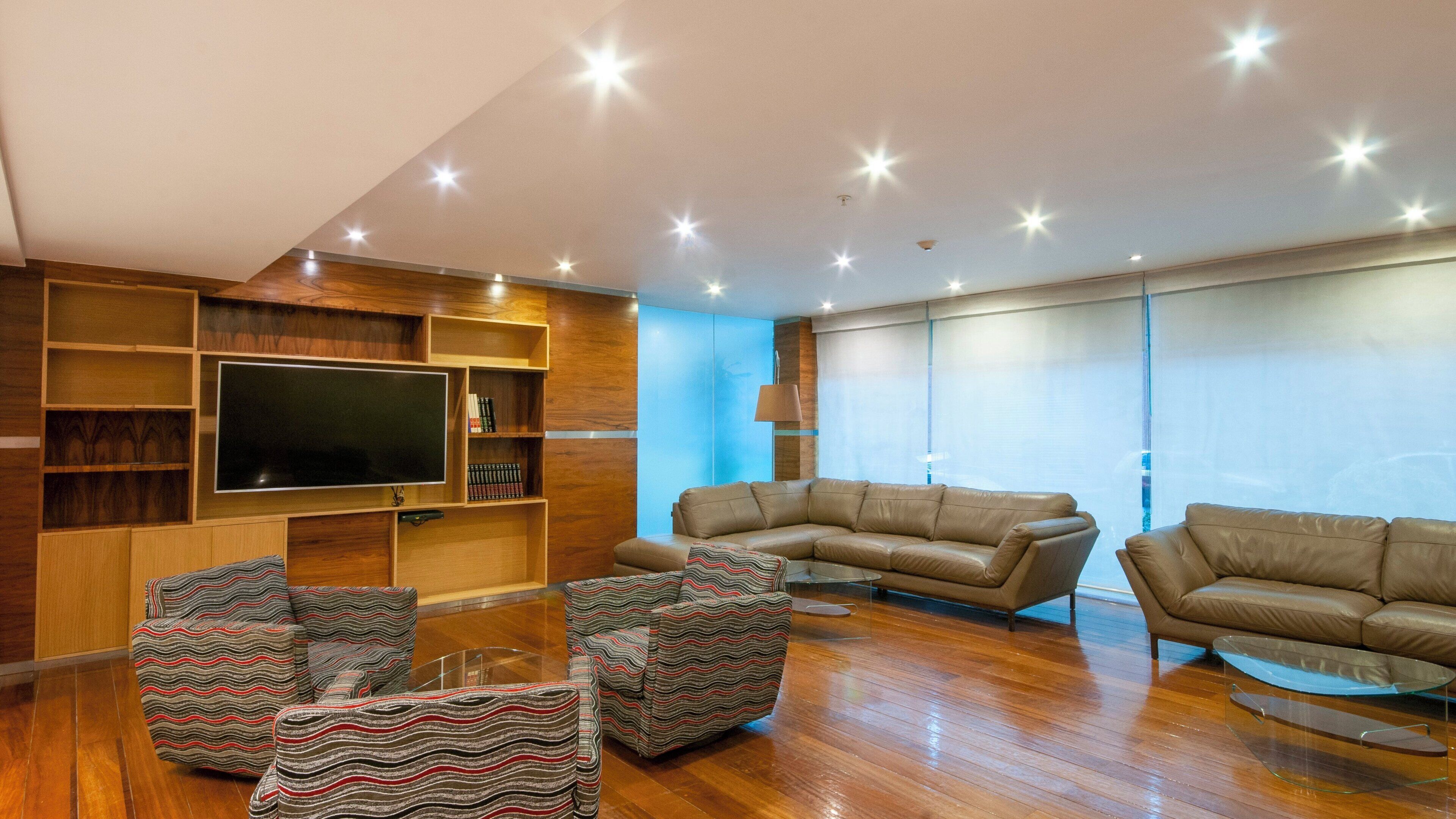 A modern living room with a large flat-screen TV, built-in shelving, leather sofas, and a patterned armchair.