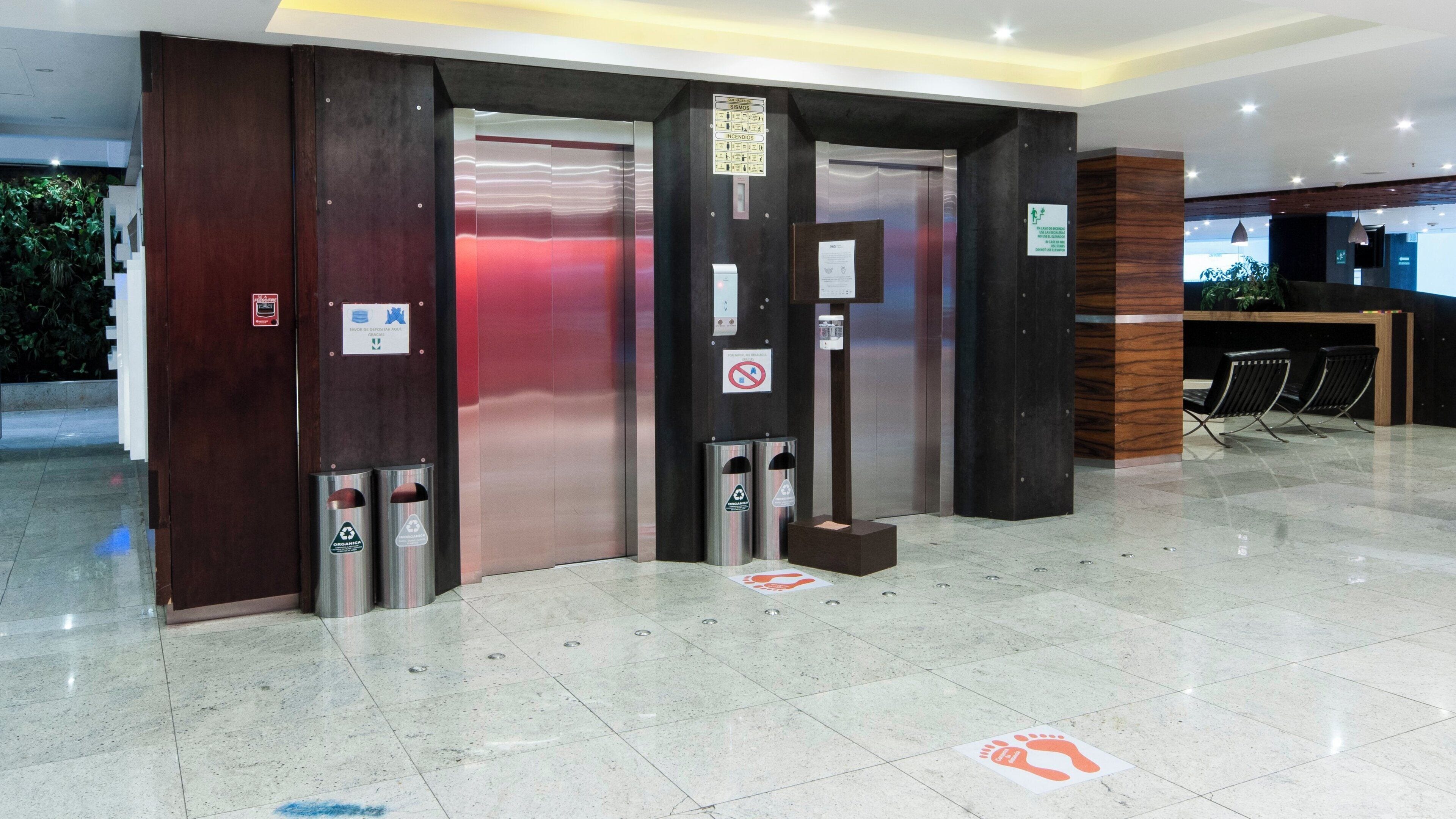 An elevator area with two elevators, a reception desk, and a trash bin.