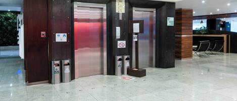An elevator area with two elevators, a reception desk, and a trash bin.