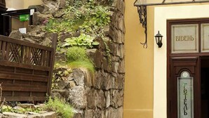 A stone wall with greenery, a wooden fence, and a building entrance with a sign reading "FOTЕA". - Wien Hotel (Lviv)