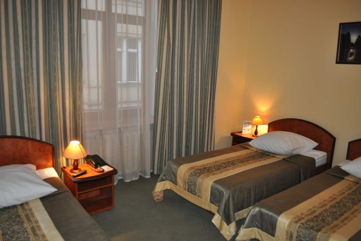 Una habitación de hotel con dos camas individuales, una mesita de noche con lámpara y una ventana con cortinas.