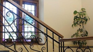 A staircase with ornate black metal railings and wooden handrails, leading to a room with a large window and potted plants. - Wien Hotel (Lviv)