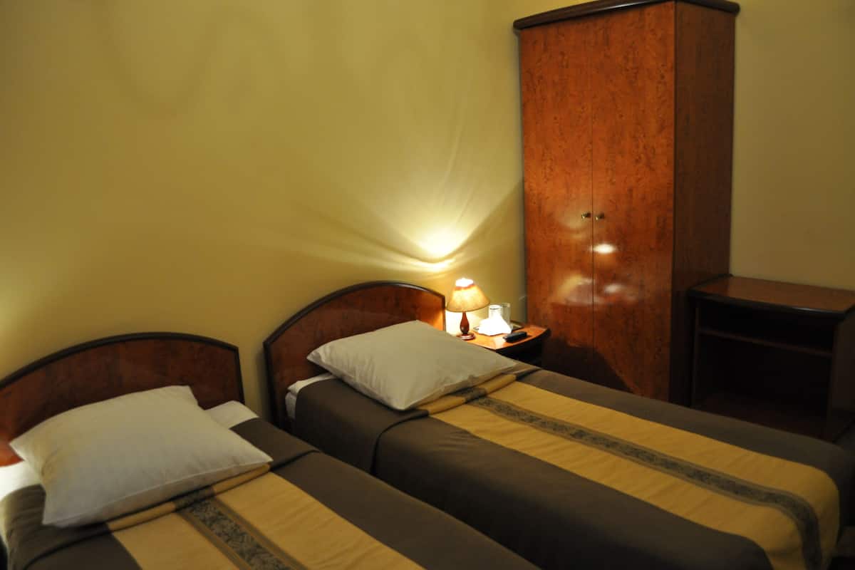 Cama doble con cabecera de madera, mesita de noche con lámpara y armario en una habitación de hotel.