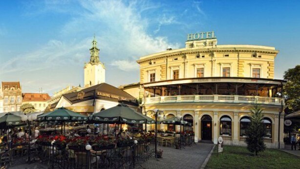 A hotel with a central courtyard, outdoor seating area, and a prominent tower in the background. - Wien Hotel (Lviv)
