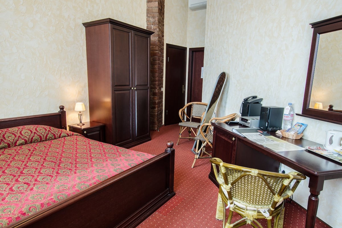 A hotel room with a bed, a desk, a chair, a wardrobe, and a mirror.