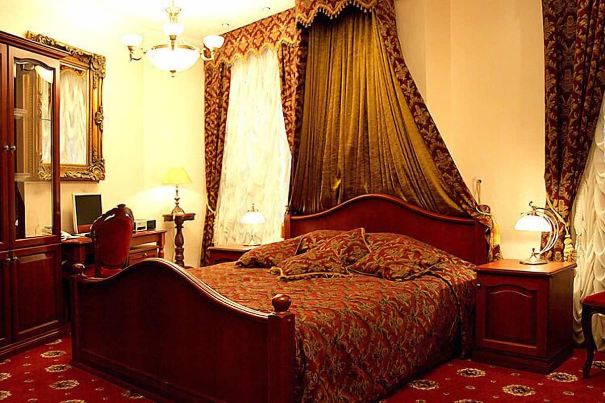 A traditional bedroom with a four-poster bed, a wooden wardrobe, a desk with a chair, and a nightstand with a lamp.