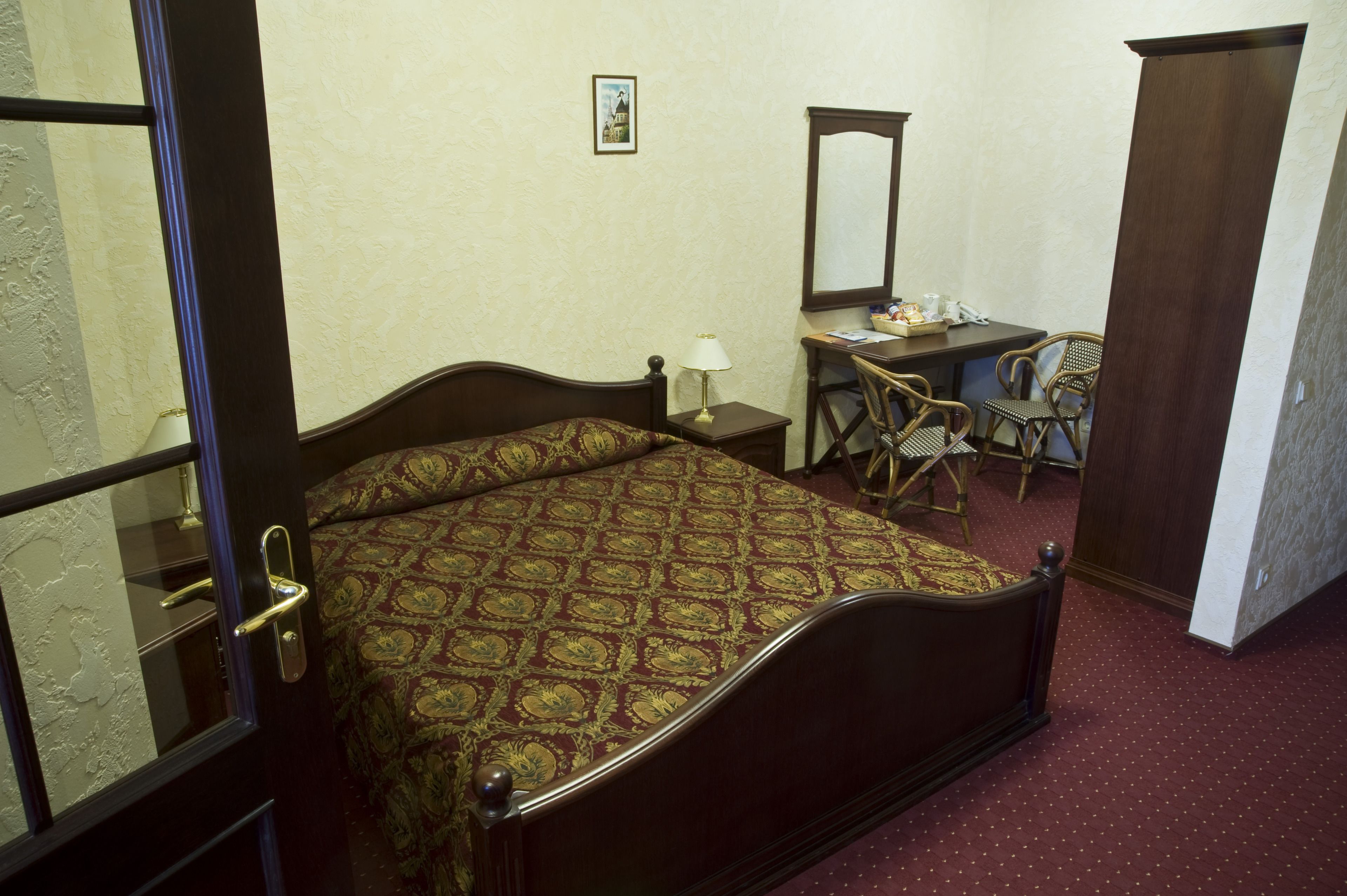 A bedroom with a bed, a desk, two chairs, a lamp, and a mirror.