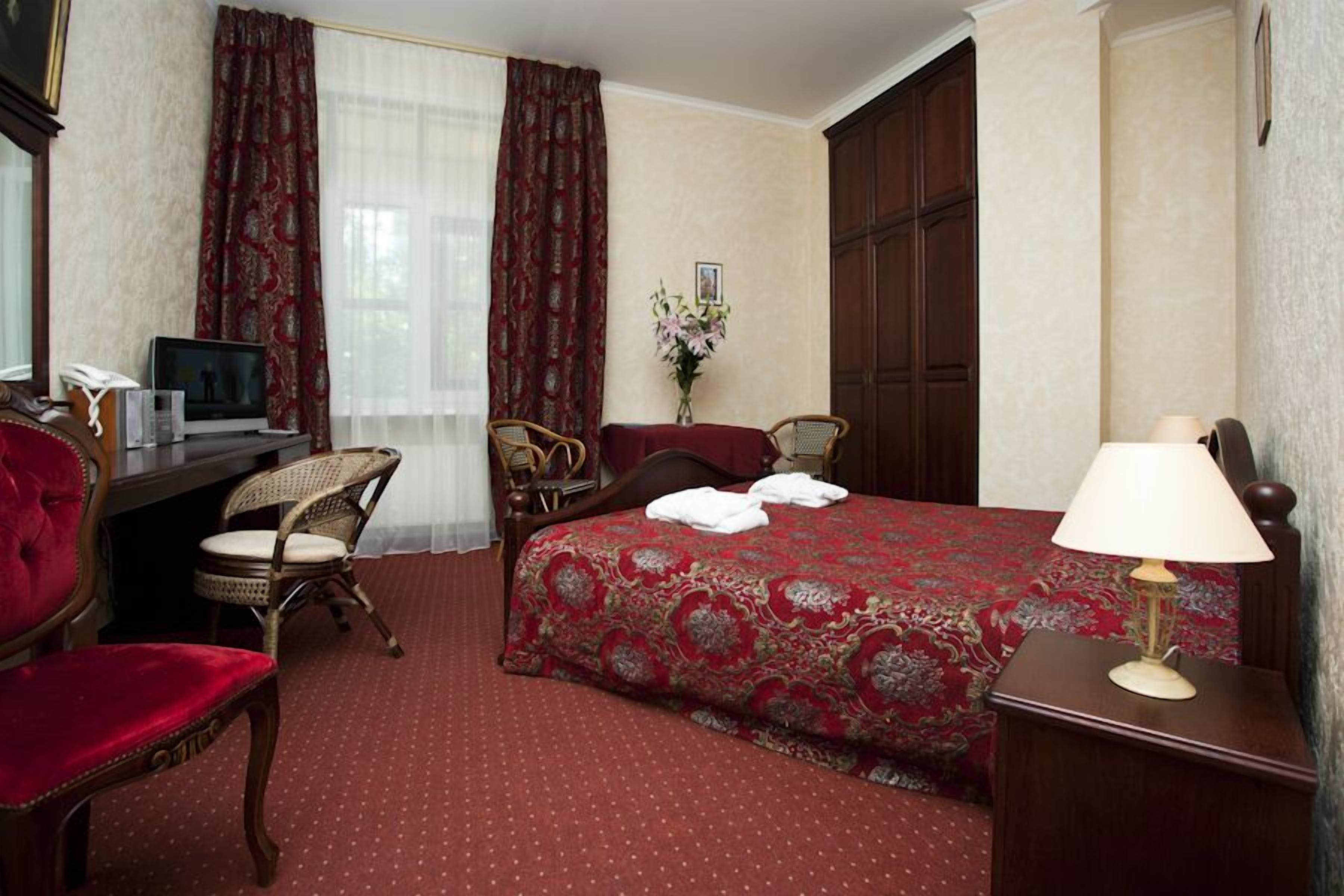 A hotel room with a bed, two chairs, a desk with a television, and a lamp.