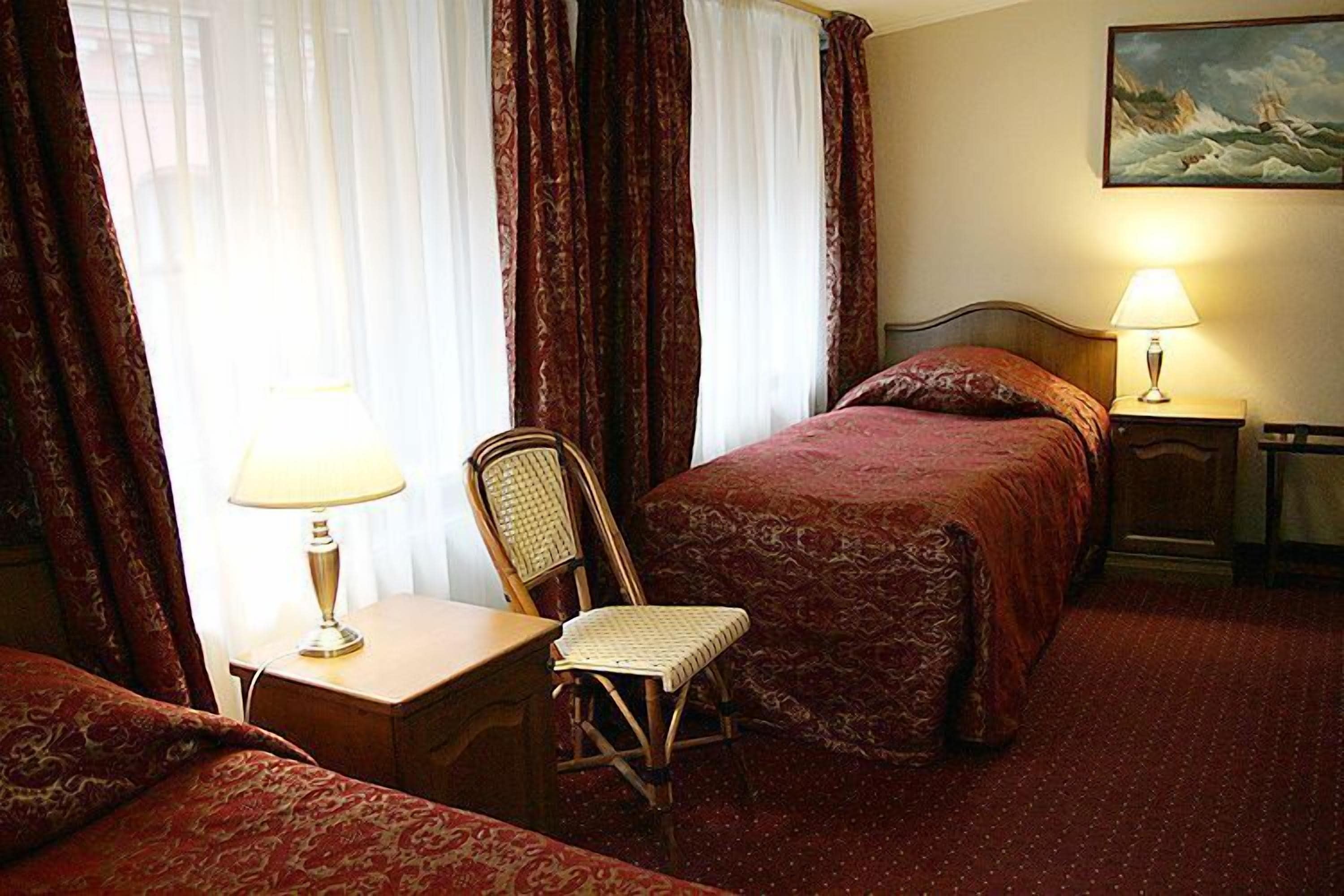 Hotellihuone, jossa on kaksi sänkyä, työpöytä, tuoli ja yöpöytä, jossa on lamput.