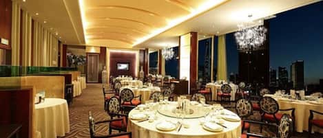 A spacious dining area with round tables and chairs, a city view, and a modern ceiling design.
