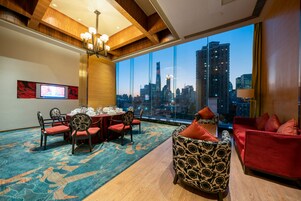 A hotel room with a city view, a dining area with a table set, and a seating area with patterned chairs and sofas.