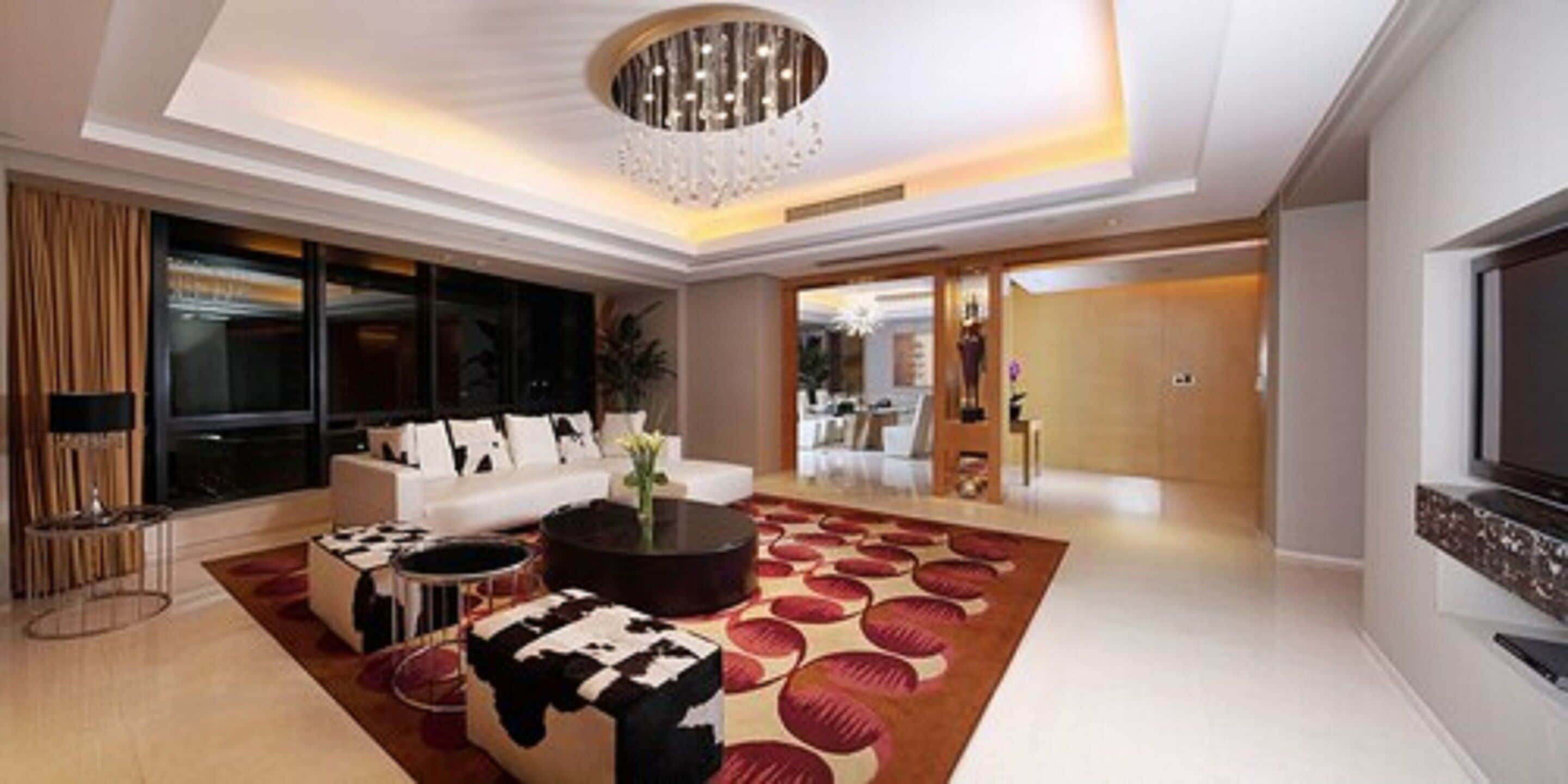A modern living room with a large TV, a white sofa, and a patterned rug.