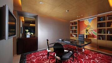 A modern room with a glass desk, a red patterned carpet, a bookshelf, and a large painting on the wall.