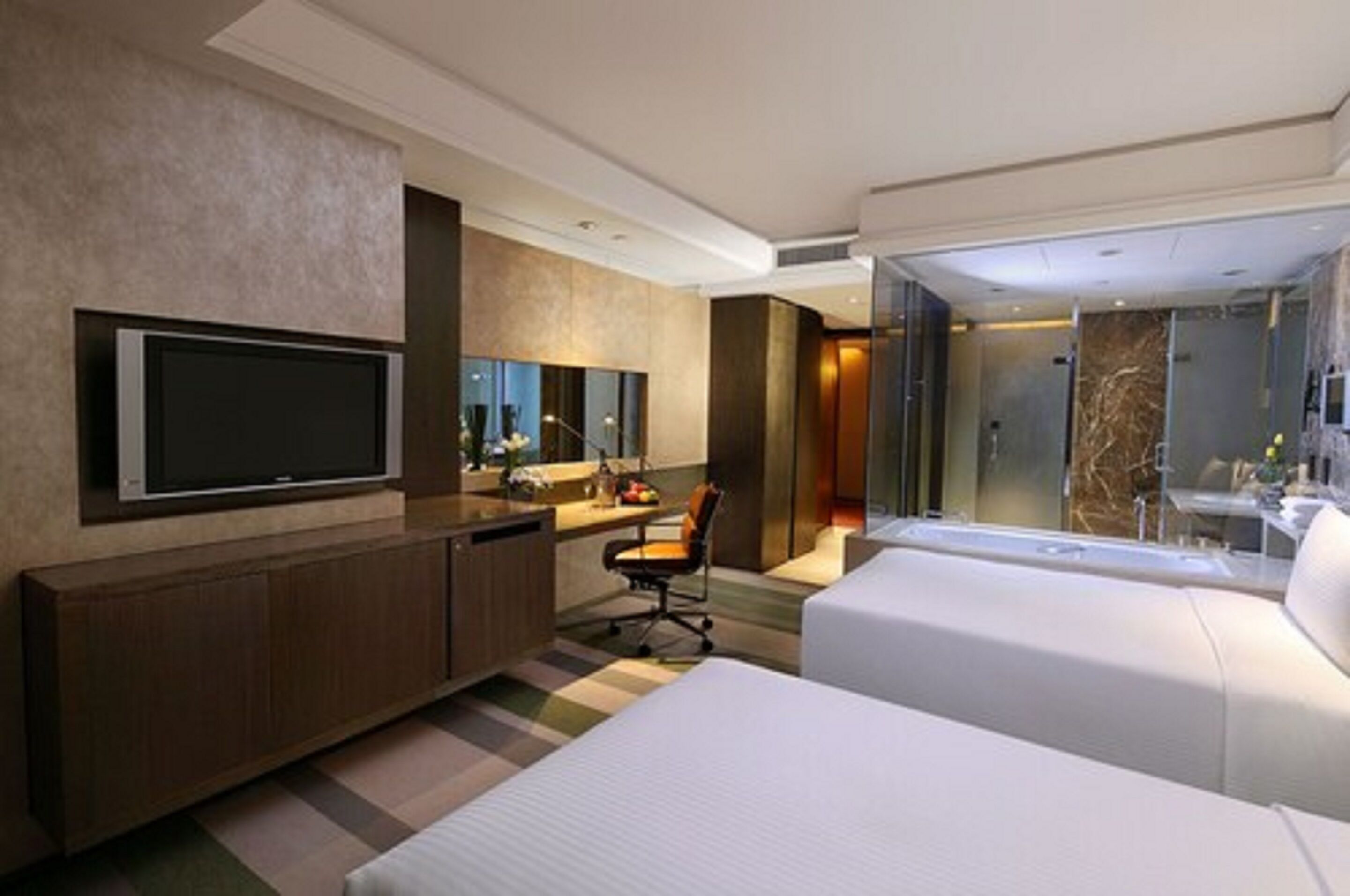 A modern hotel room with a large bed, a desk with a chair, a television, and a bathroom with a glass shower.