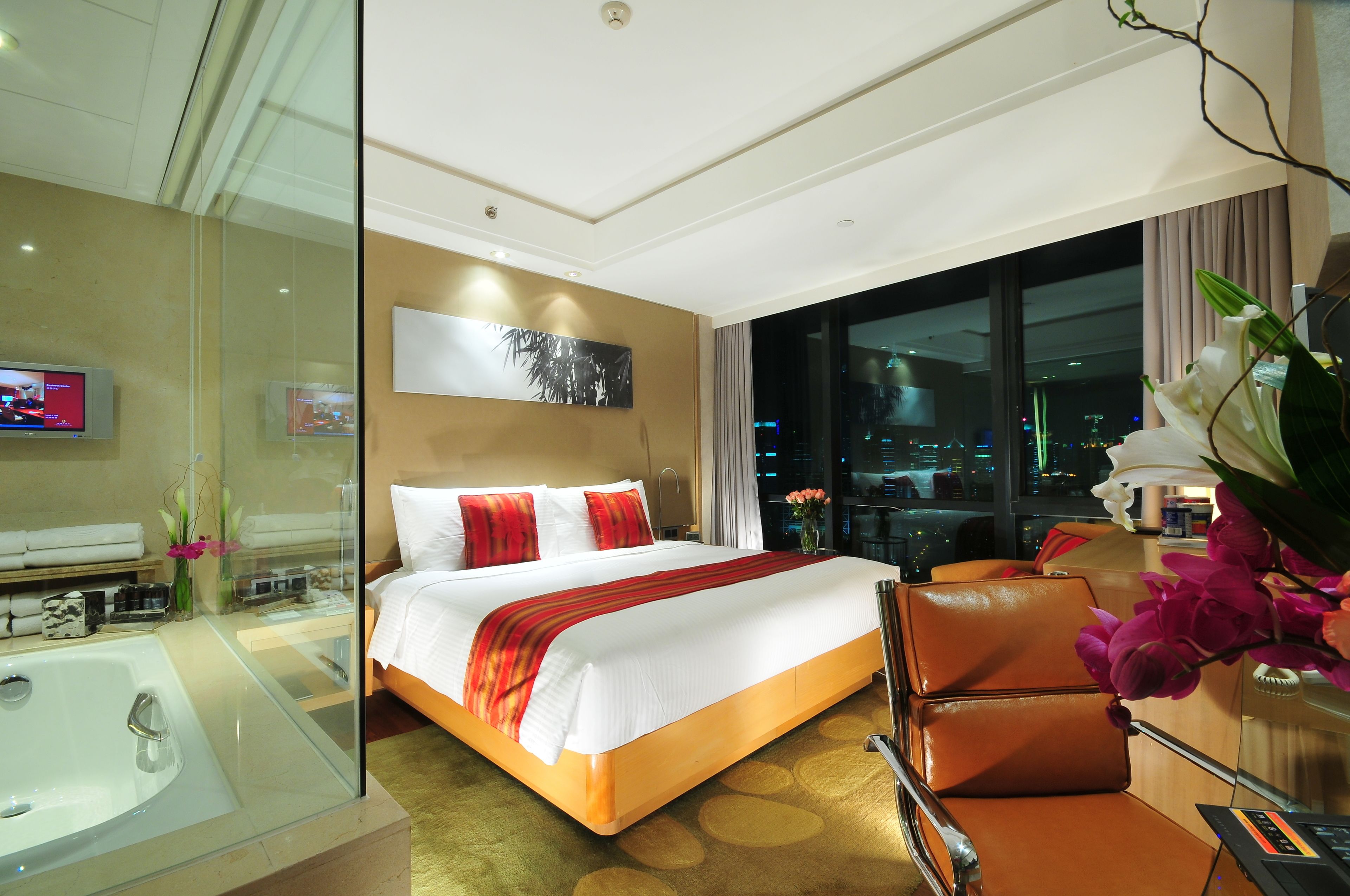 Una habitación de hotel con una cama grande, baño con paredes de vidrio, vista a la ciudad y una decoración moderna.