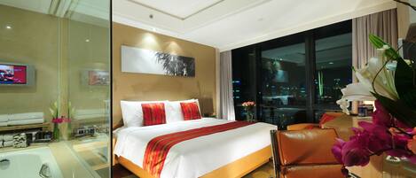 A hotel room with a large bed, a glass-enclosed bathroom, a city view, and a modern decor.