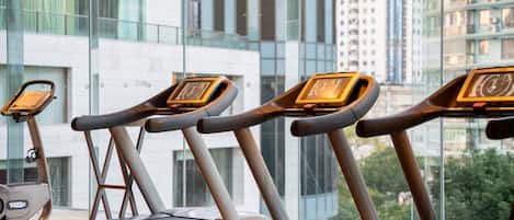 Eine Reihe von Laufbändern in einem Fitnessstudio mit Blick auf moderne Gebäude und Grünflächen.