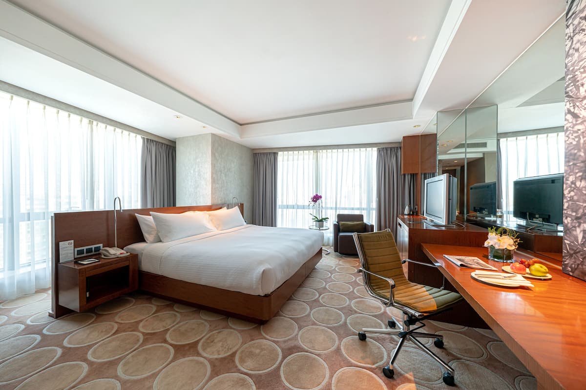A hotel room with a large bed, a desk with a chair, a TV, and a small table with flowers.