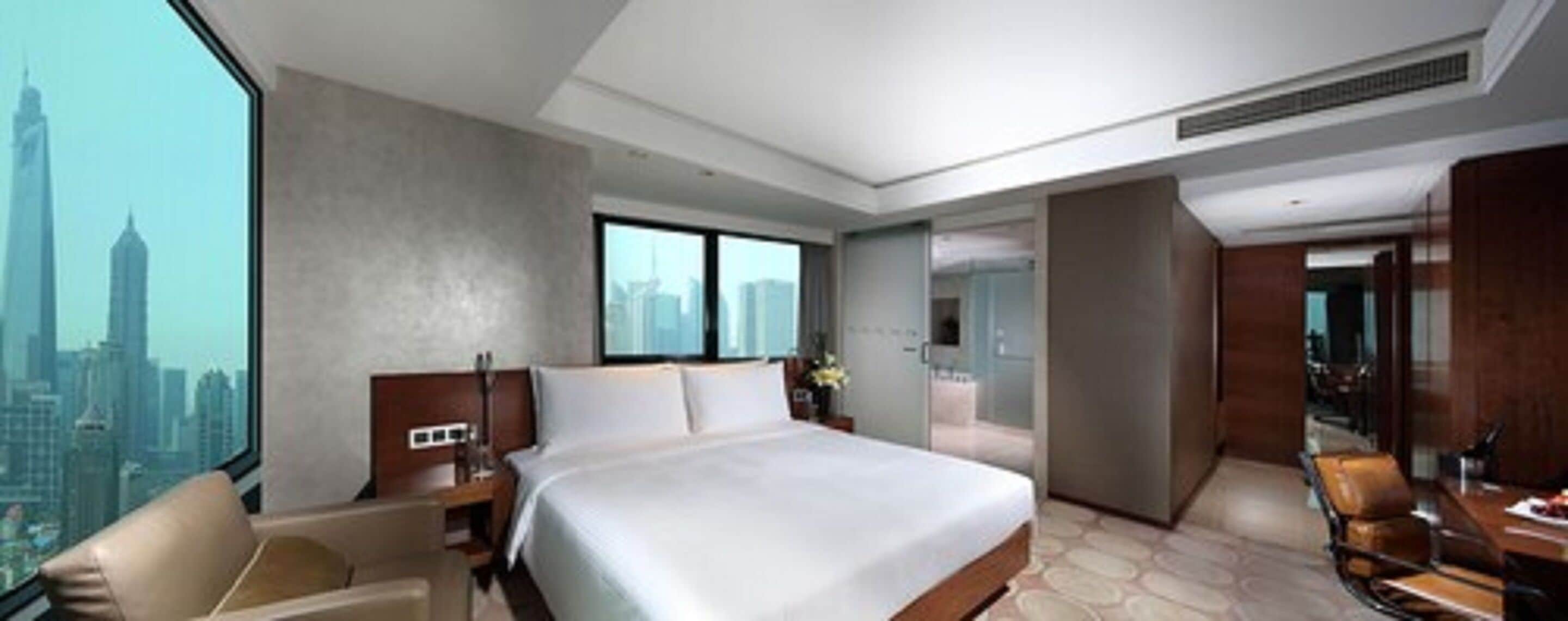 A hotel room with a large bed, a desk, and a view of a cityscape.